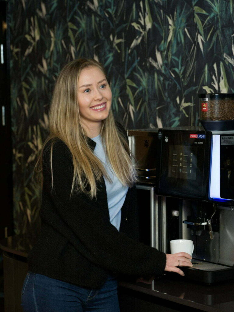 Jente med langt lyst hår foran kaffemaskin