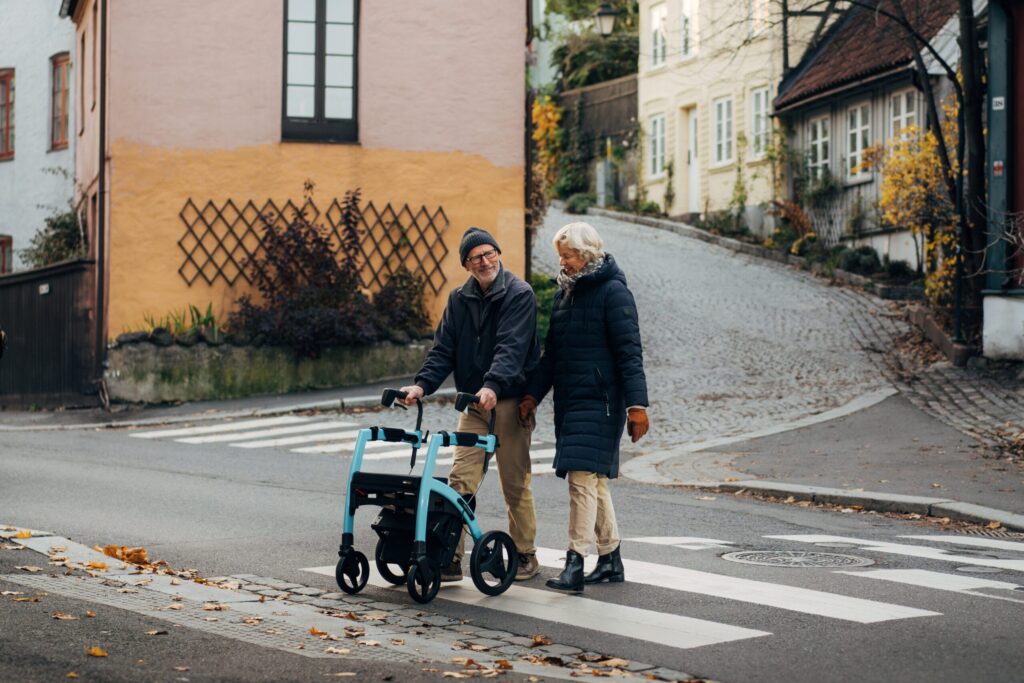 Äldre par går över ett övergångsställe. Mannen använder en rollator.