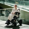 Laila sitter i en elektrisk rullstol från Elio. Hon poserar framför kameran i ett köpcentrum.