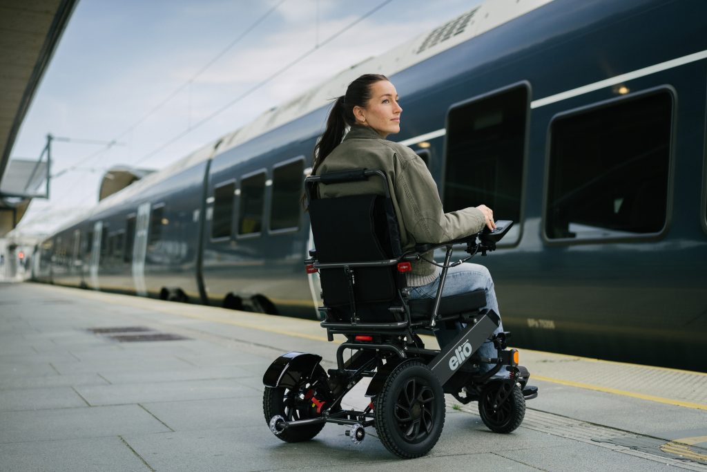 Kvinna i en Elio elektrisk rullstol på en tågperrong, med ett tåg i bakgrunden